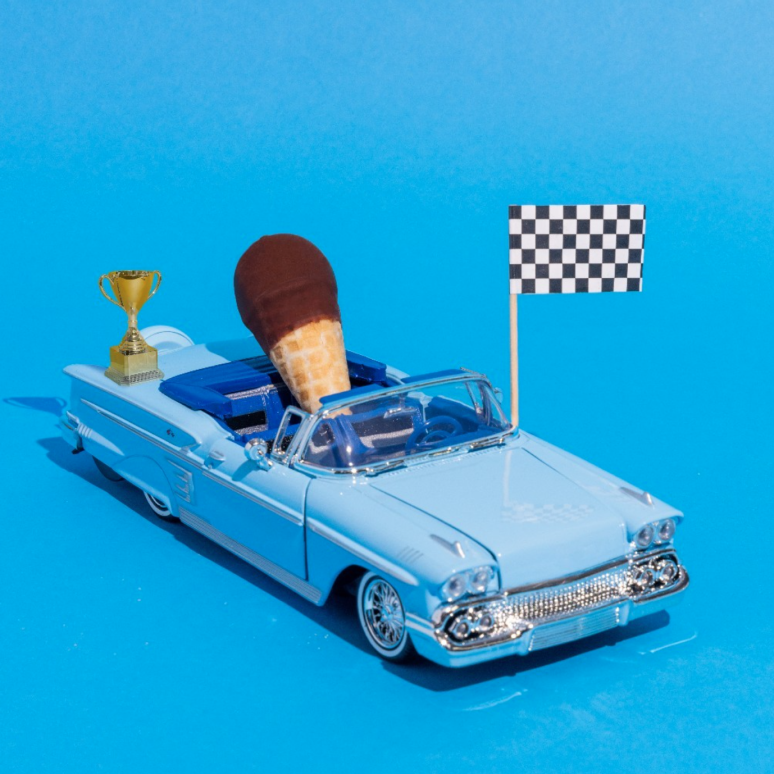A toy car with a Drumstick mini cone in the front seat. 