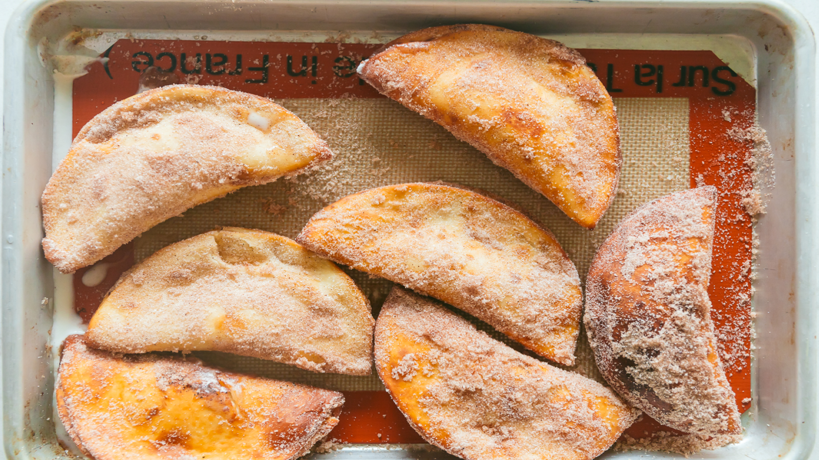 Seven finished butter pecan frozen dairy dessert empanadas covered in sugar on a tray.