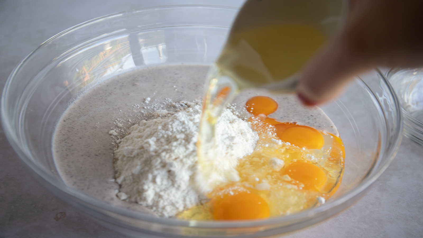 Close up of a bowl filled with melted Cookies 'N Cream frozen dairy dessert, eggs, and flow with someone pouring more eggs in.