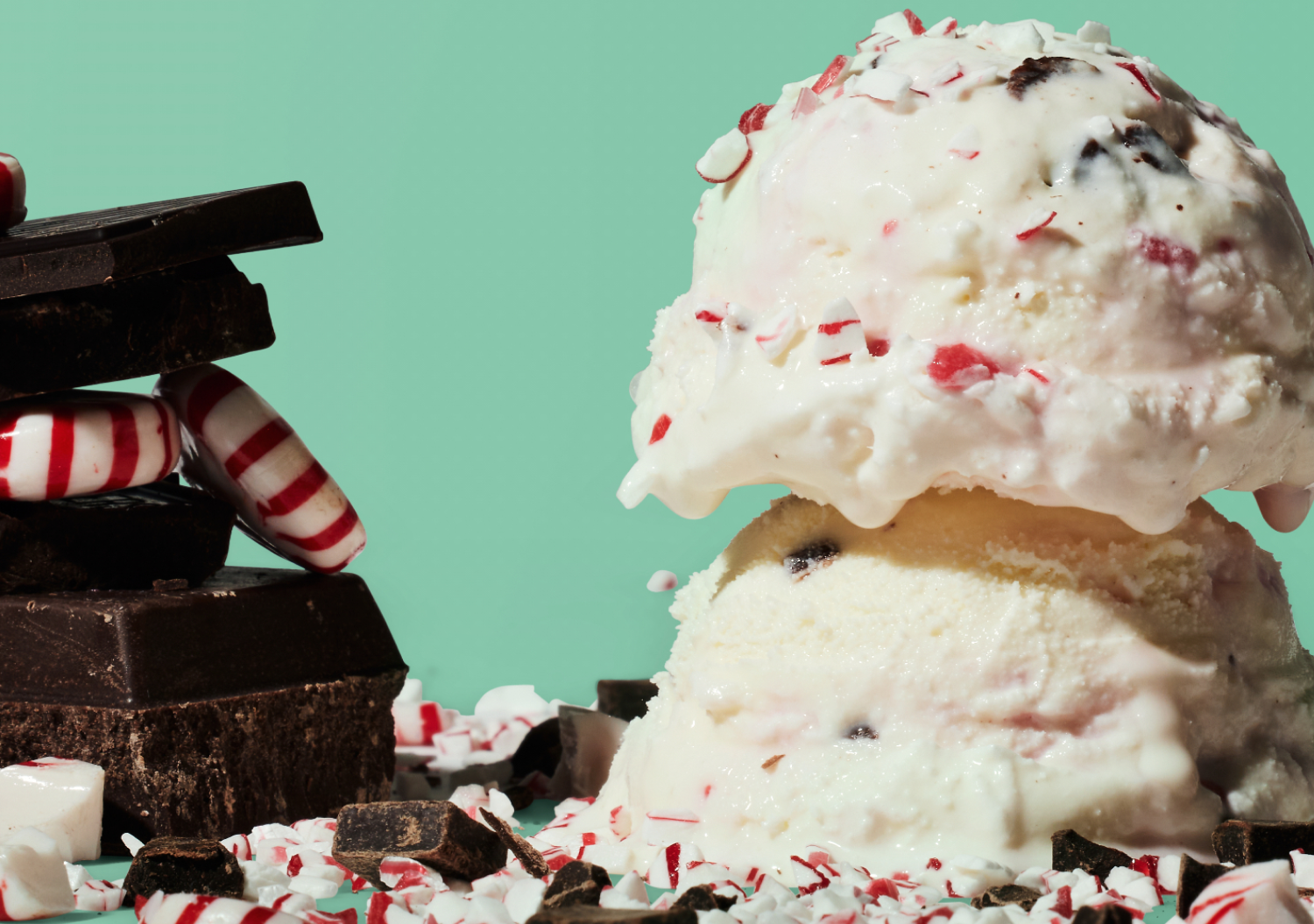 Two scoops of peppermint bark ice cream next to pieces of chocolate and peppermints. 