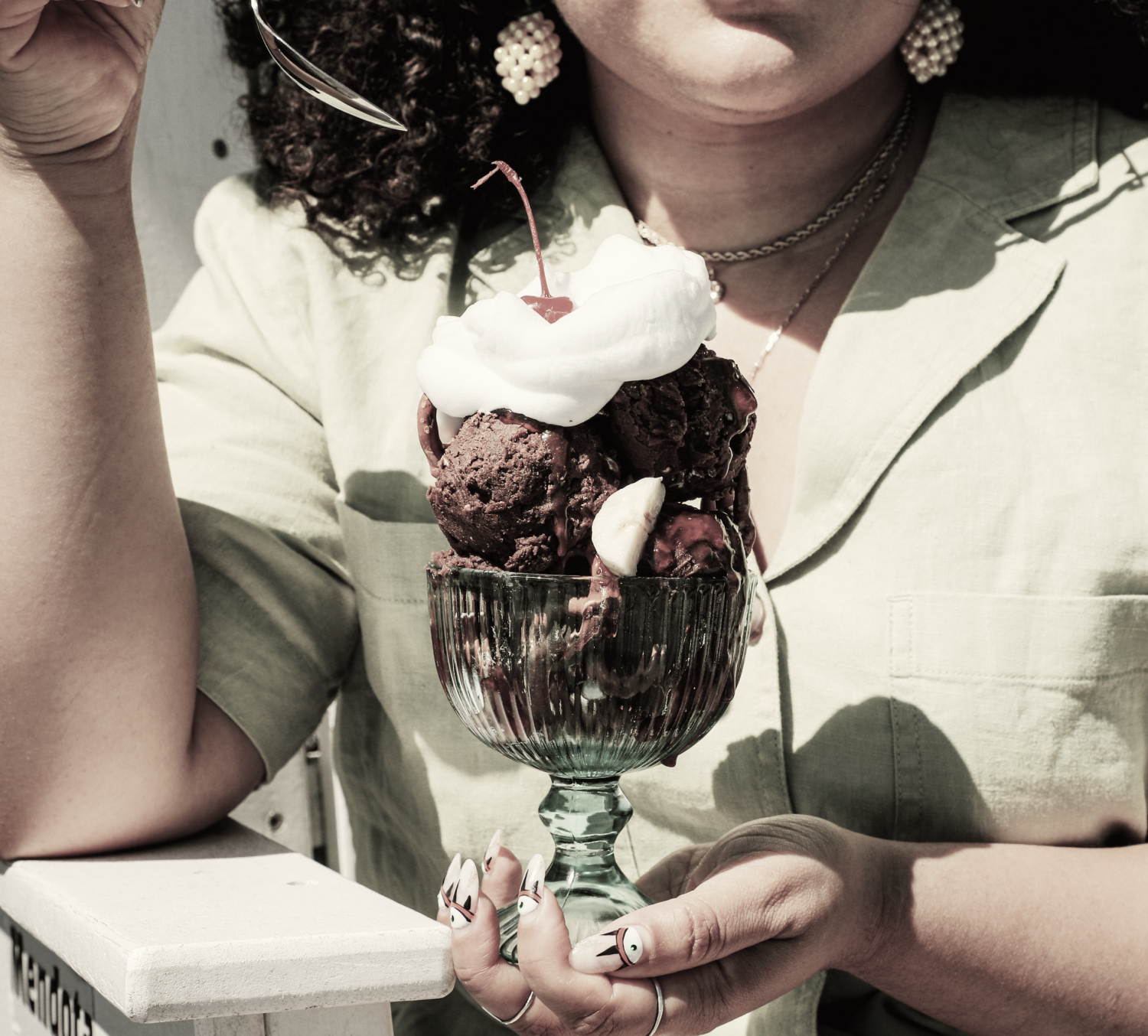 Closeup of a woman holding up a vintage ice cream sundae topped with whipped cream and a cherry. 