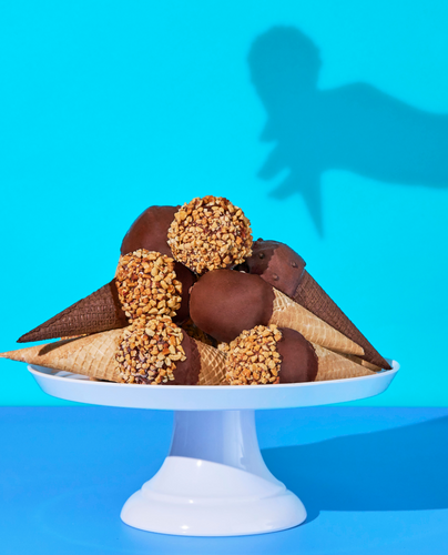 A plate full of various Drumstick cones, some coated in peanuts, others in chocolate. 
