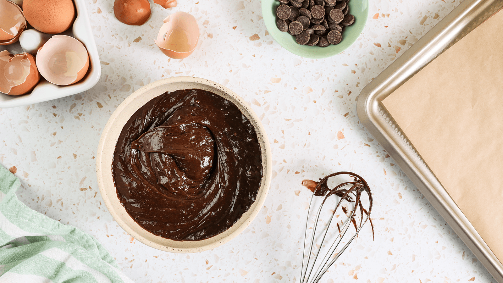 Chocolate cake mix in a bowl on a countertop with a cracked egg and whisk besides it.