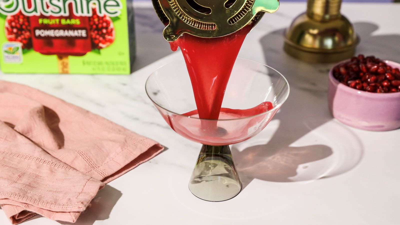 Straining a red witches brew halloween mocktail into a martini glass.