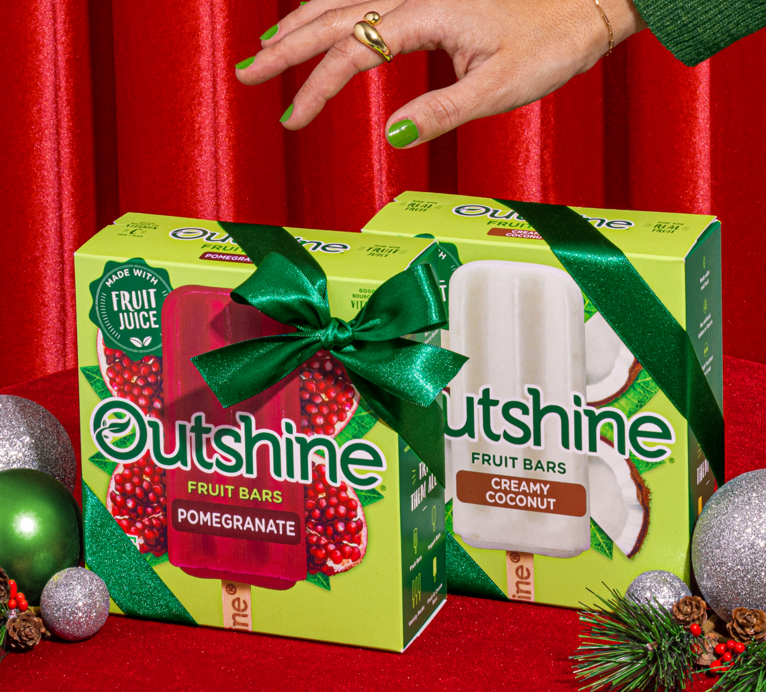 Two boxes of Outshine frozen fruit bars with ribbons and bows surrounded by ornaments.