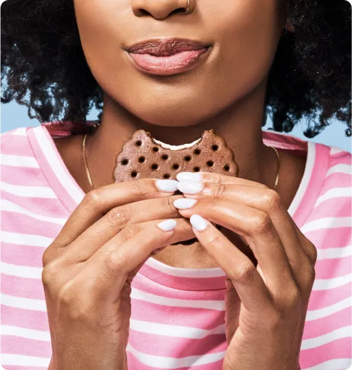 A closeup of a woman taking a bite of a Skinny Cow ice cream sandwich
